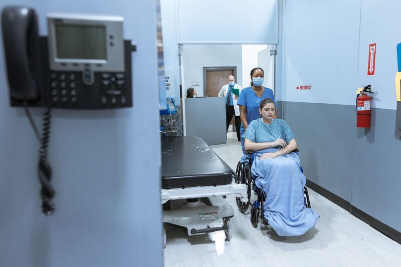 A nurse helping a patient in a wheelchair along a hospital corridor