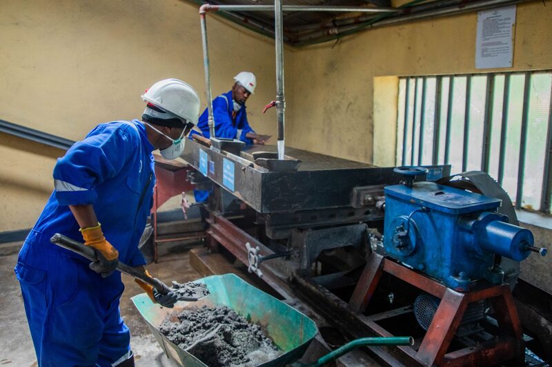 Two workers in helmets and overalls operating machinery in a workshop